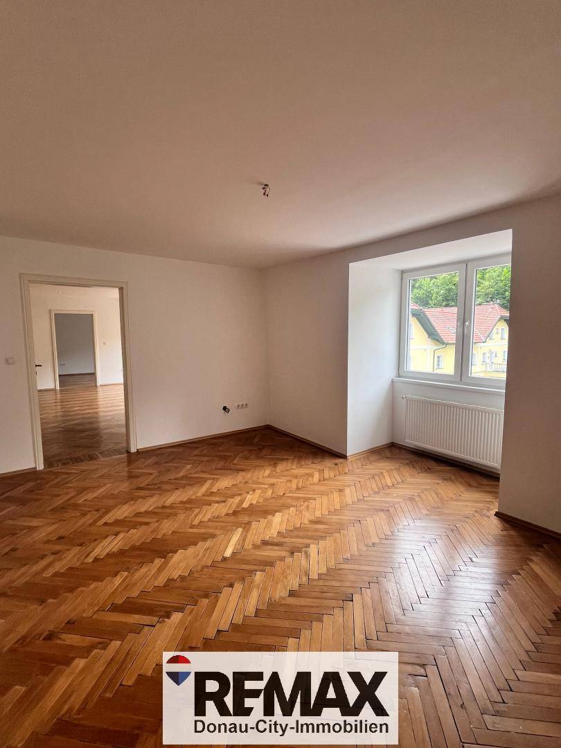 Geräumiger Wohnbereich mit Fischgrätparkett und einem großen Fenster für viel Tageslicht.