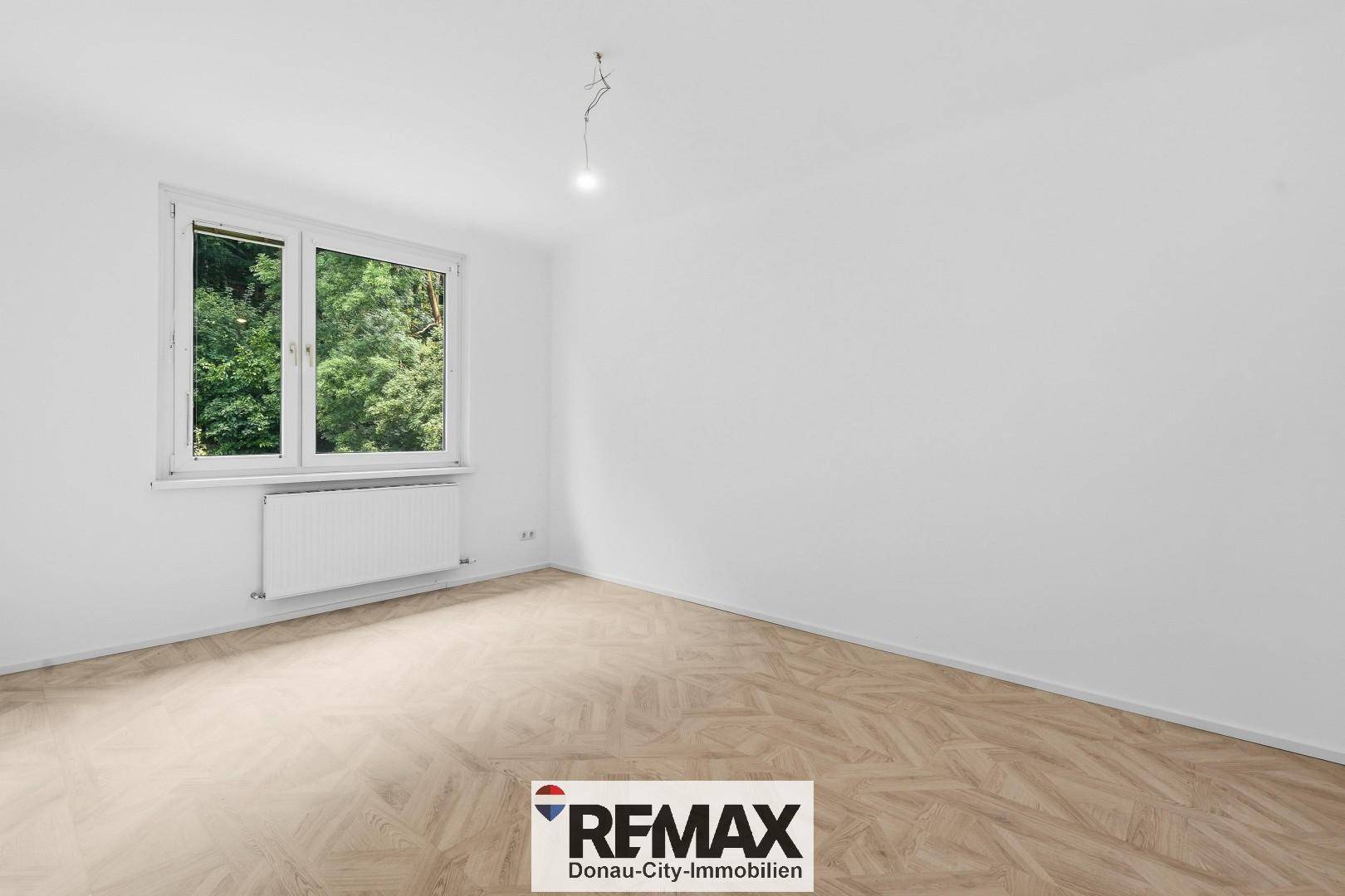 Geräumiges Zimmer mit hellem Parkettboden und Fenster mit Blick auf die umliegende Natur.