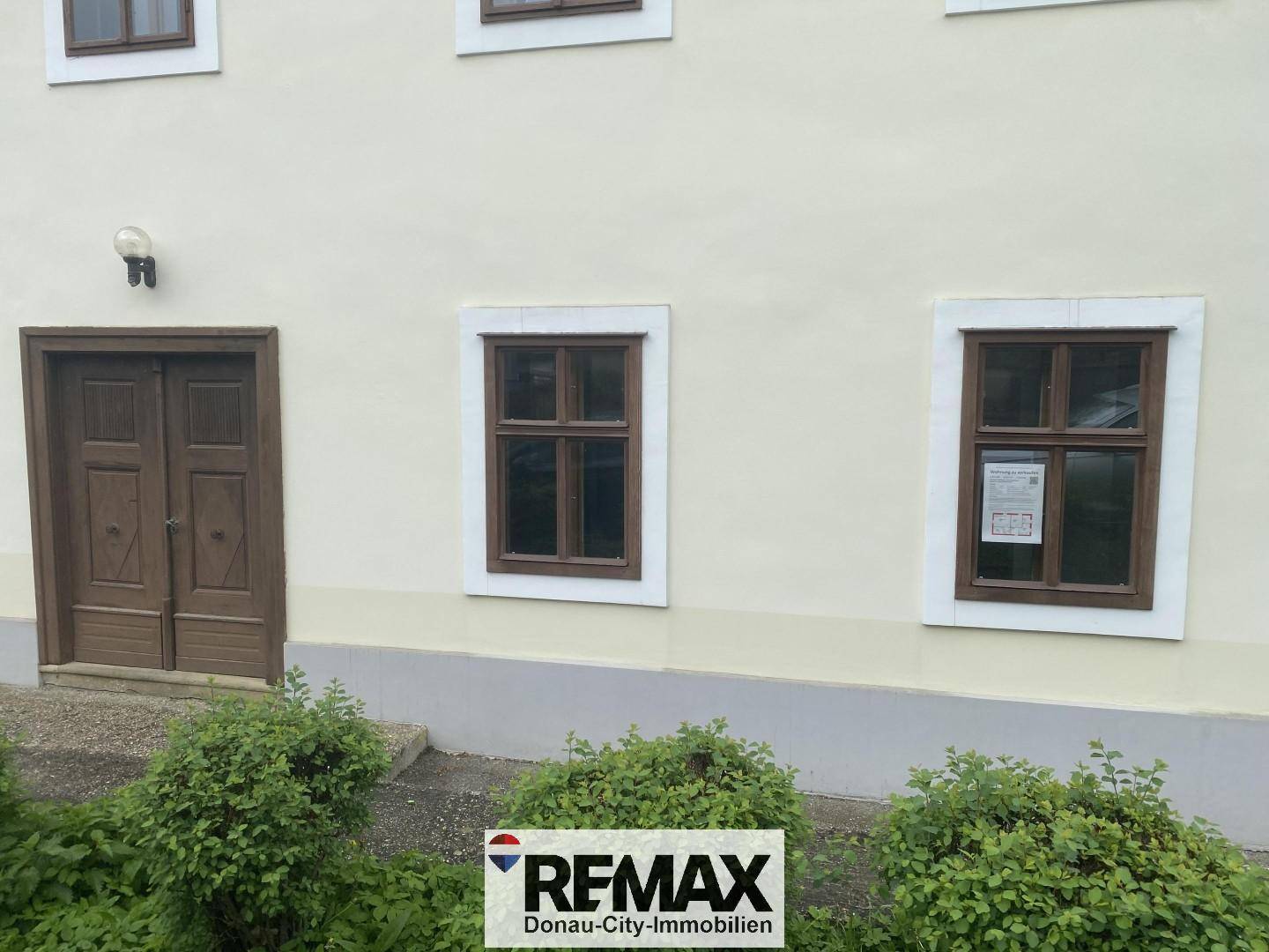 Detailansicht der Fassade mit Holztür und Fenstern, umgeben von gepflegten Büschen.