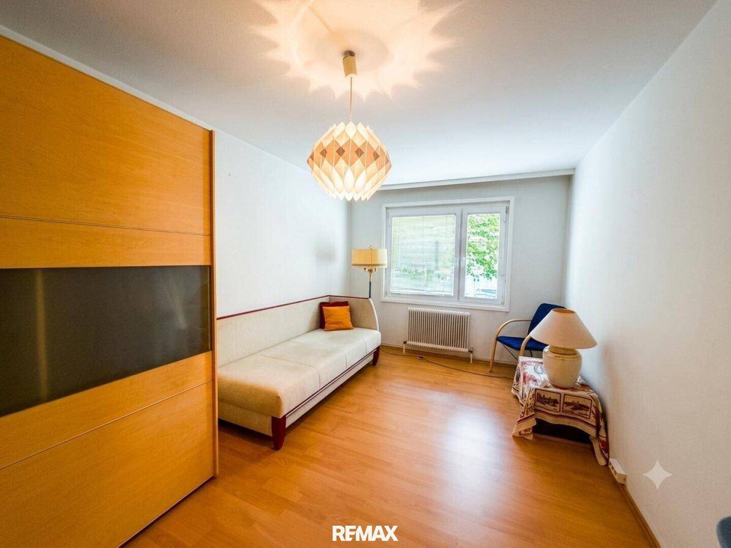 Gemütliches Zimmer mit Sofa, Holzschrank und Fenster mit Blick ins Grüne.