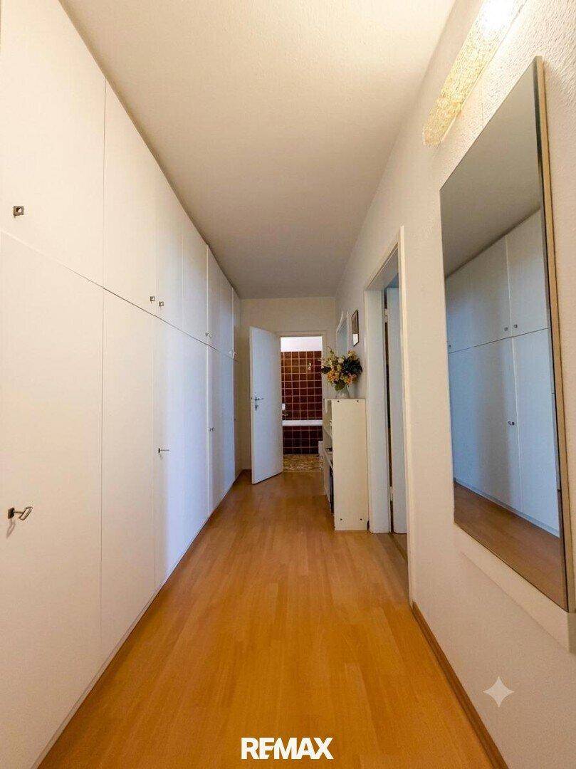 Langer Flur mit Einbauschränken, Spiegel und Holzboden.