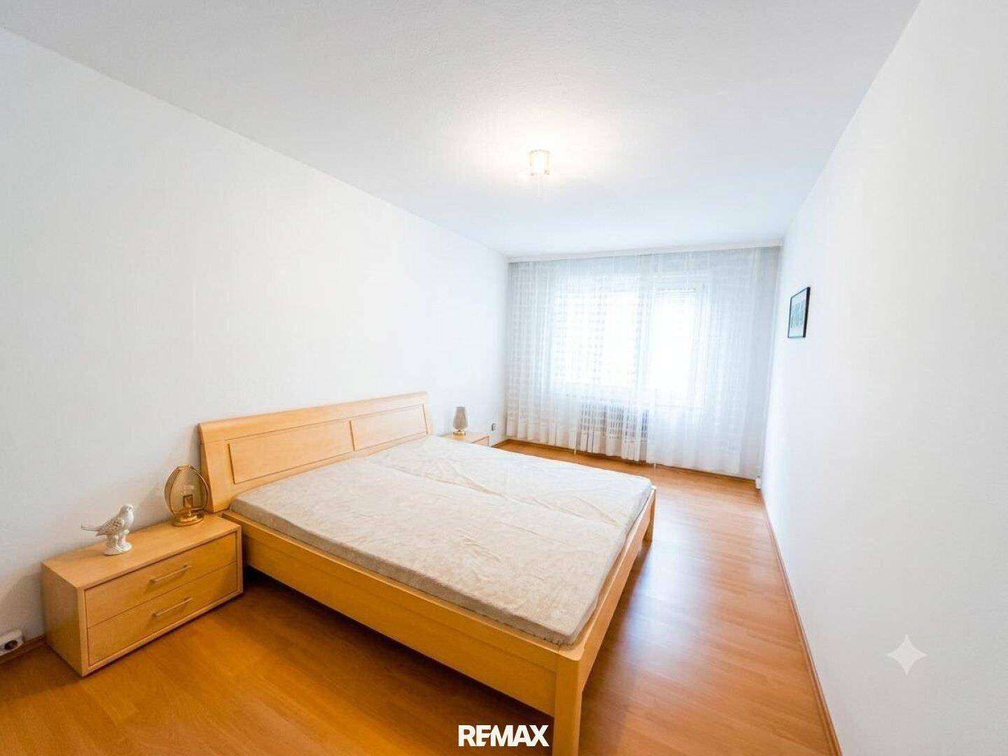 Helles Schlafzimmer mit Doppelbett, Nachttischen und großem Fenster.