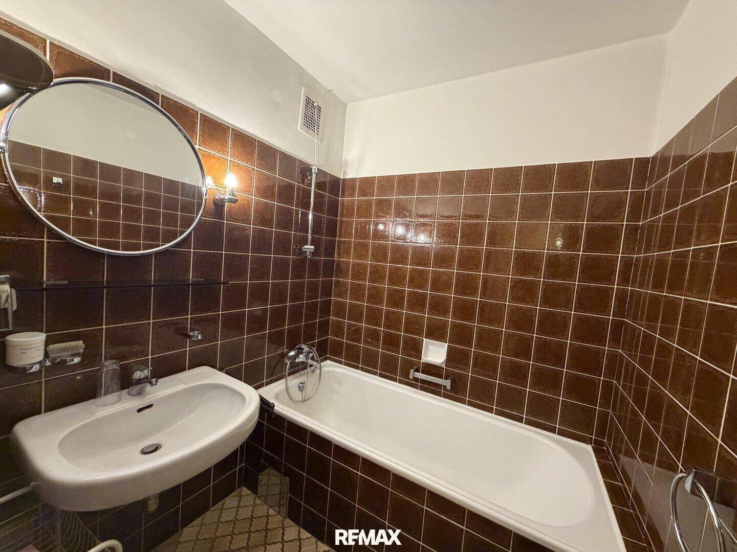 Badezimmer mit braunen Fliesen, Badewanne und Waschbecken.