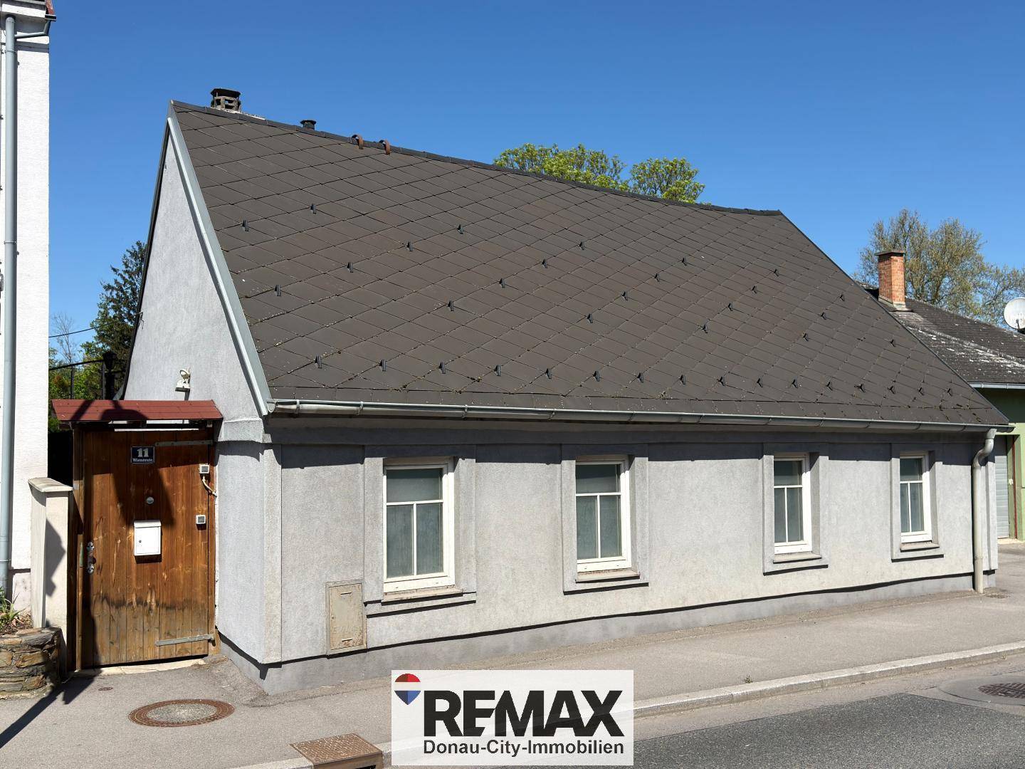 Fassade eines älteren Hauses mit Satteldach und einfachen Fenstern, direkt an einer ruhigen Straße gelegen.