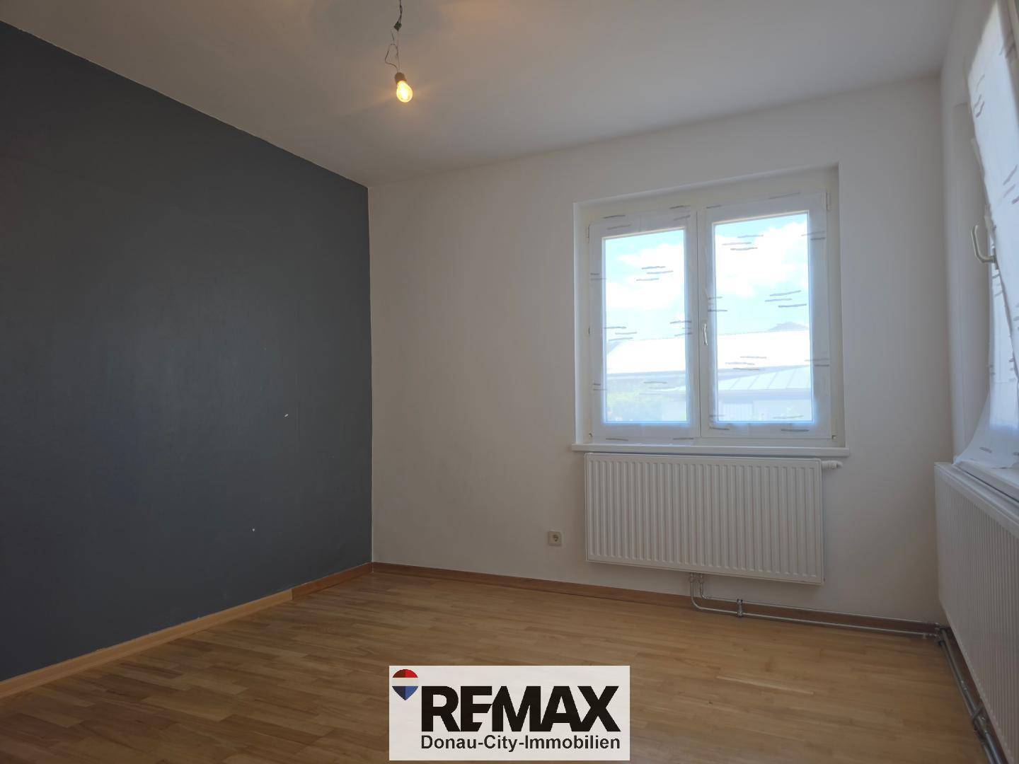 Zimmer mit einer dunkelgrauen Akzentwand und Parkettboden, beleuchtet durch ein großes Fenster.