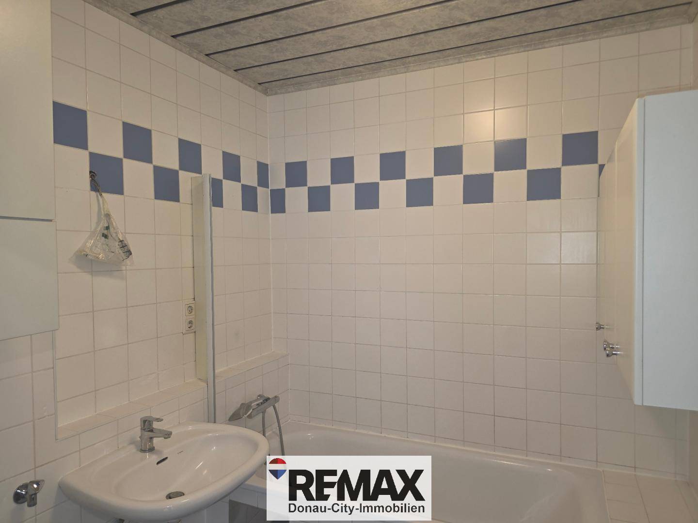 Badezimmer mit Badewanne, Waschbecken und weiß-blauen Fliesen im Schachbrettmuster.