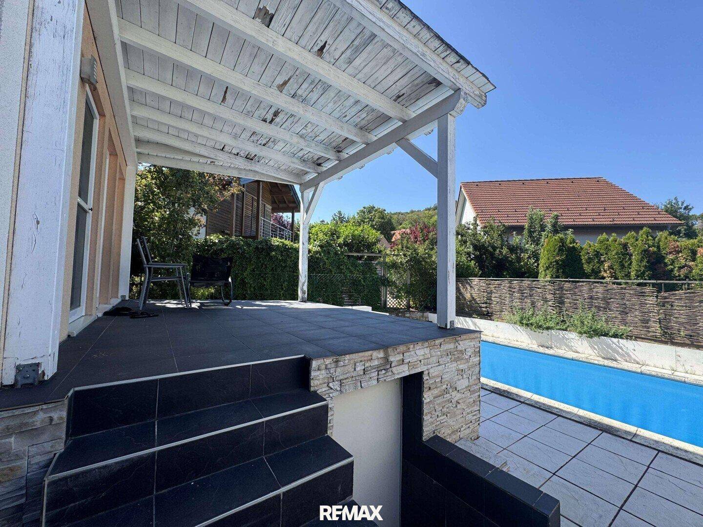 Überdachte Terrasse mit Fliesenboden und Blick auf den Pool im Garten.