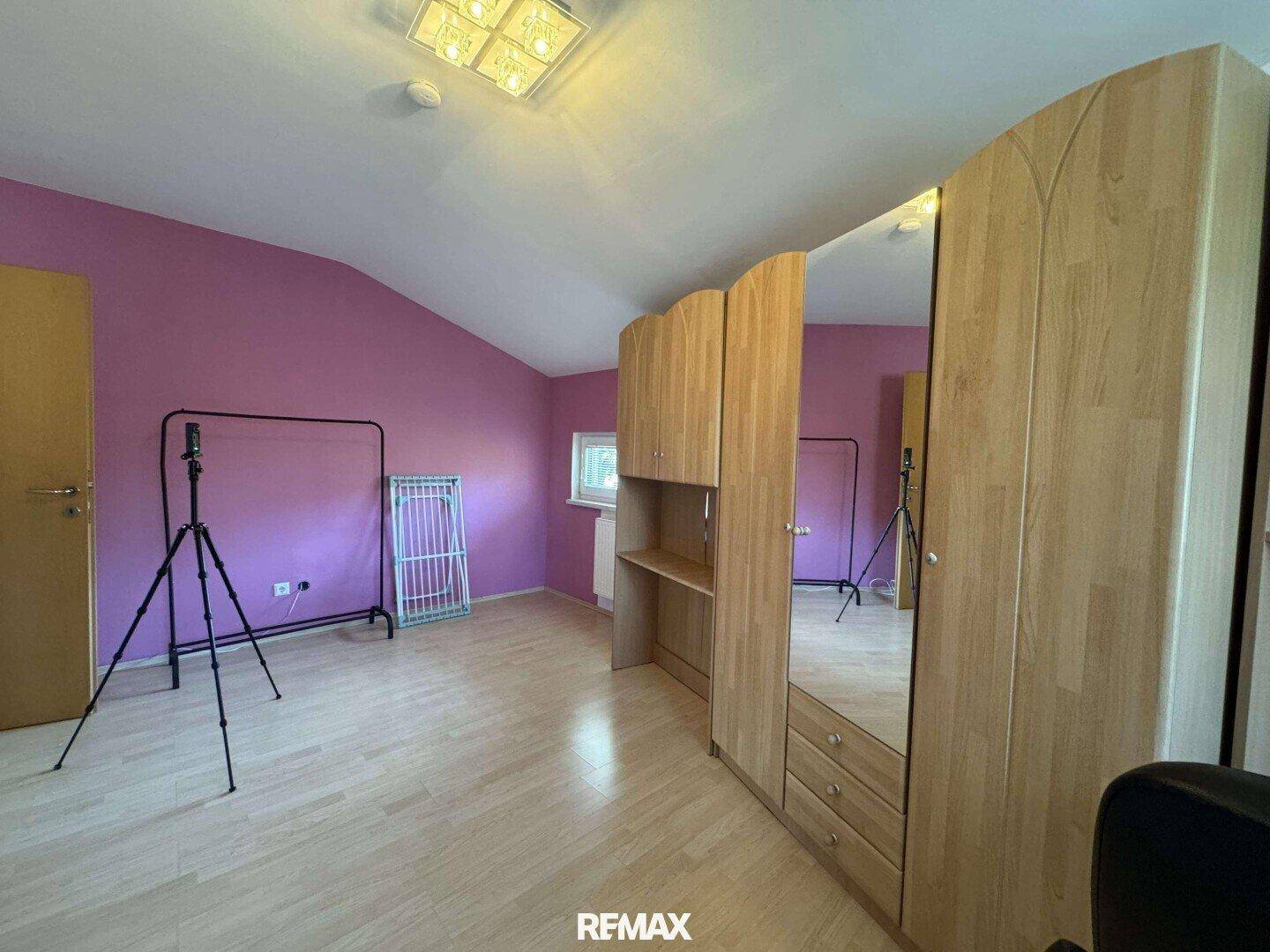 Geräumiges Zimmer mit lila Wänden, Holzboden und Kleiderschrank.