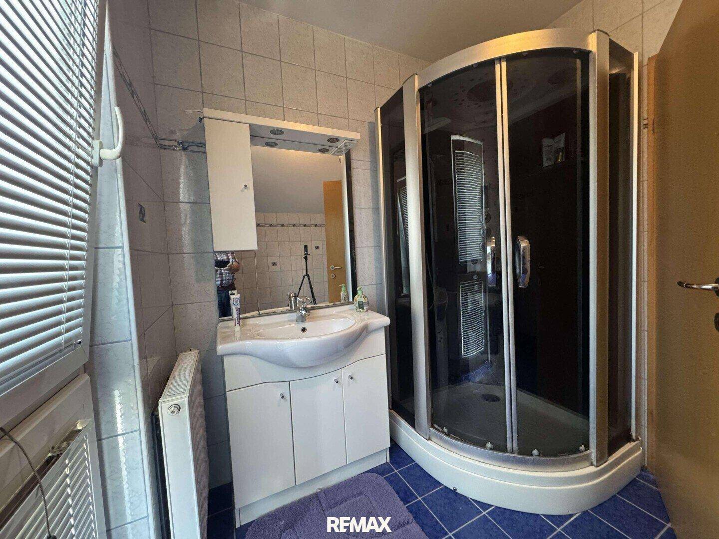 Badezimmer mit Duschkabine, Waschbecken und blauen Bodenfliesen.