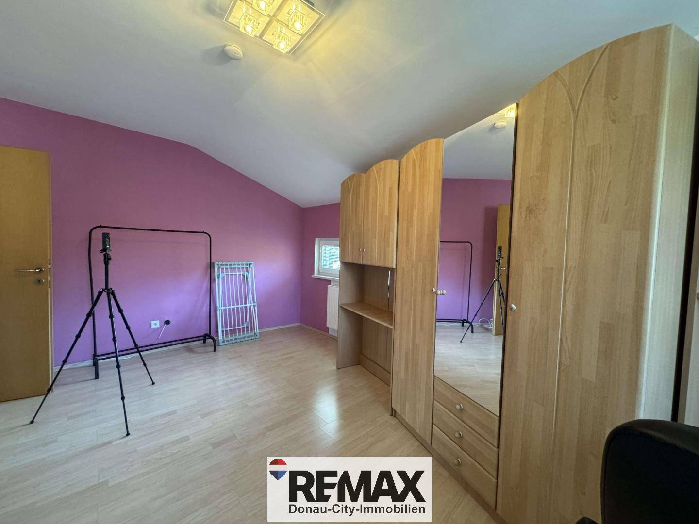 Geräumiges Zimmer mit farbigen Wänden, Holzschrank und hellem Laminatboden.