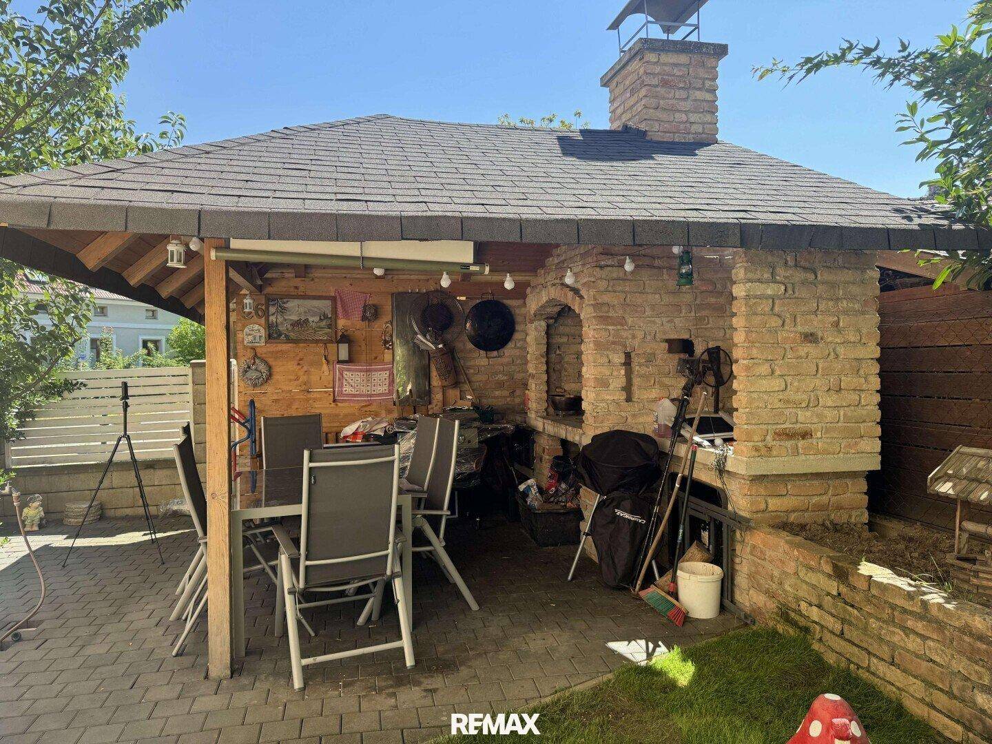 Gemütlicher Grillbereich im Garten mit überdachtem Sitzplatz und gemauertem Ofen.