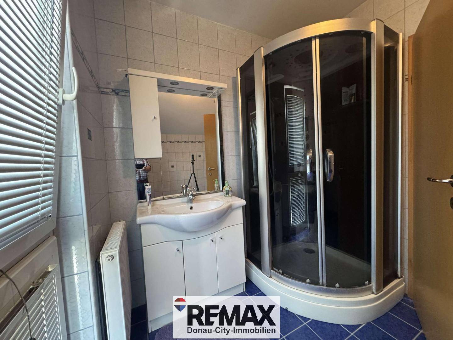 Badezimmer mit Eckdusche, Einzelwaschbecken und blauen Bodenfliesen.