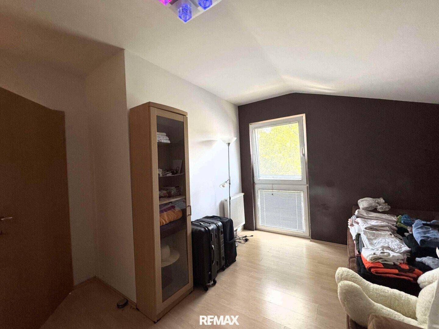 Schlafzimmer mit dunkler Akzentwand, Holzboden und Fenster.