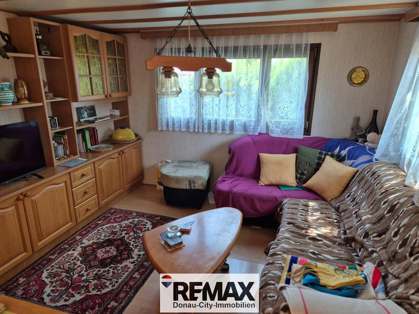 Wohnzimmer mit Sofa, Holzmöbeln und einem Fenster mit Blick ins Grüne.