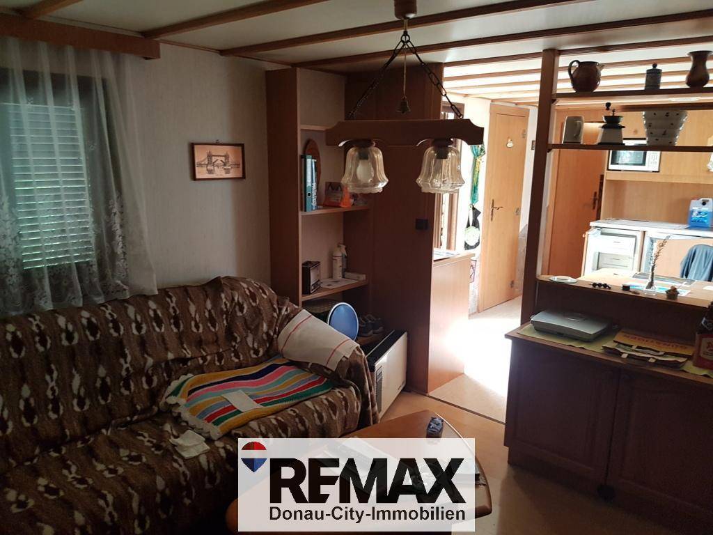 Rustikales Wohnzimmer mit Sofa, Holzbalkendecke und Durchgang zur Küche.