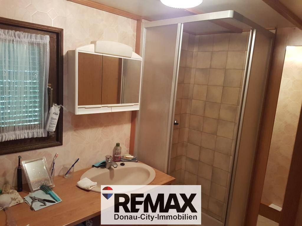 Kleines Badezimmer mit Duschkabine, Waschbecken und Spiegelschrank in einfacher Ausführung.