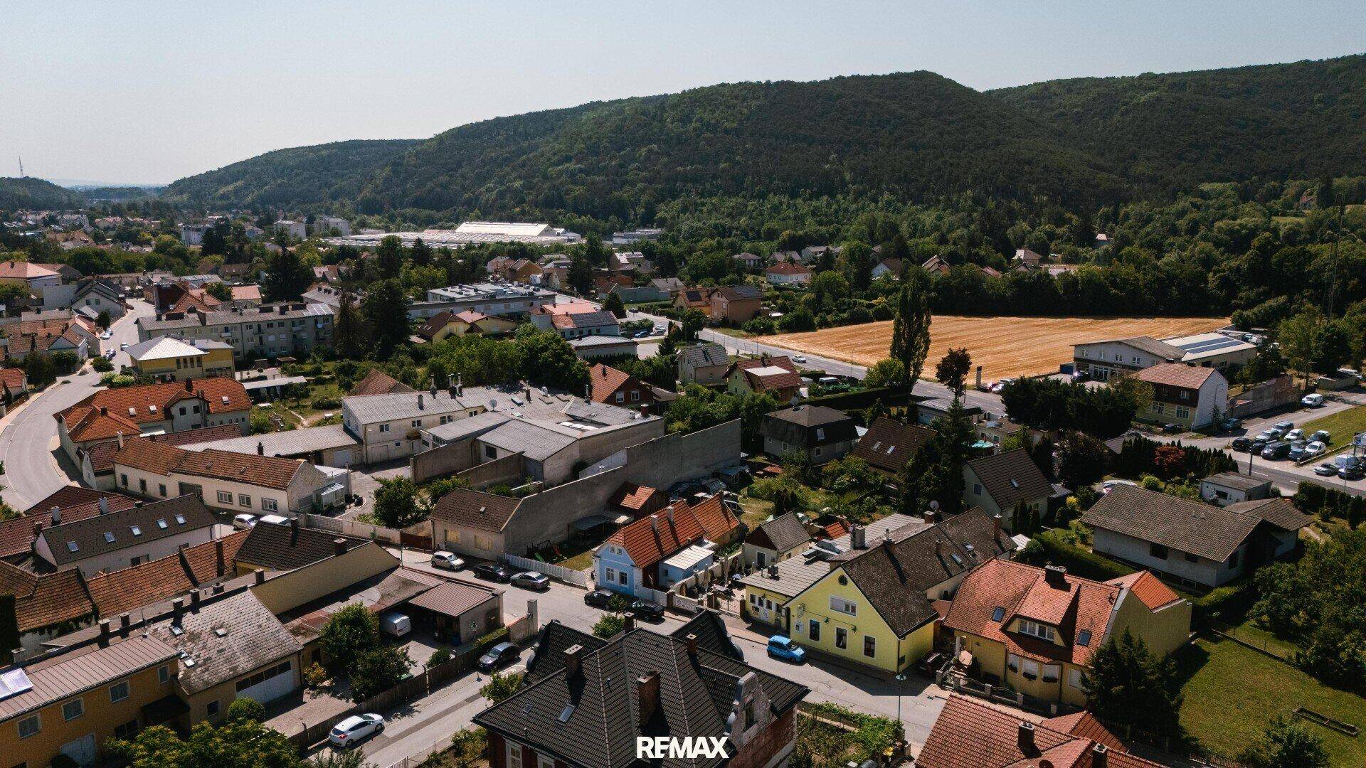 Weitläufige Luftaufnahme der Wohngegend mit Häusern, Hügeln und Feldern unter blauem Himmel.