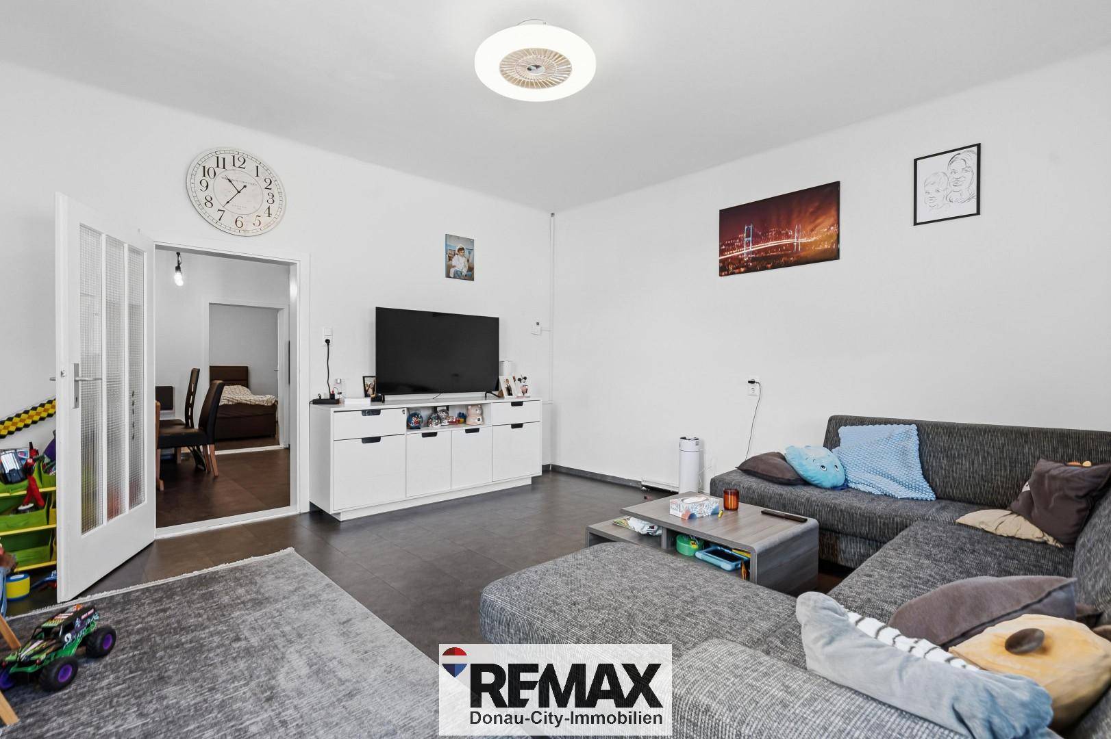 Gemütliches Wohnzimmer mit dunklem Boden, großem Sofa und Blick in ein angrenzendes Zimmer.