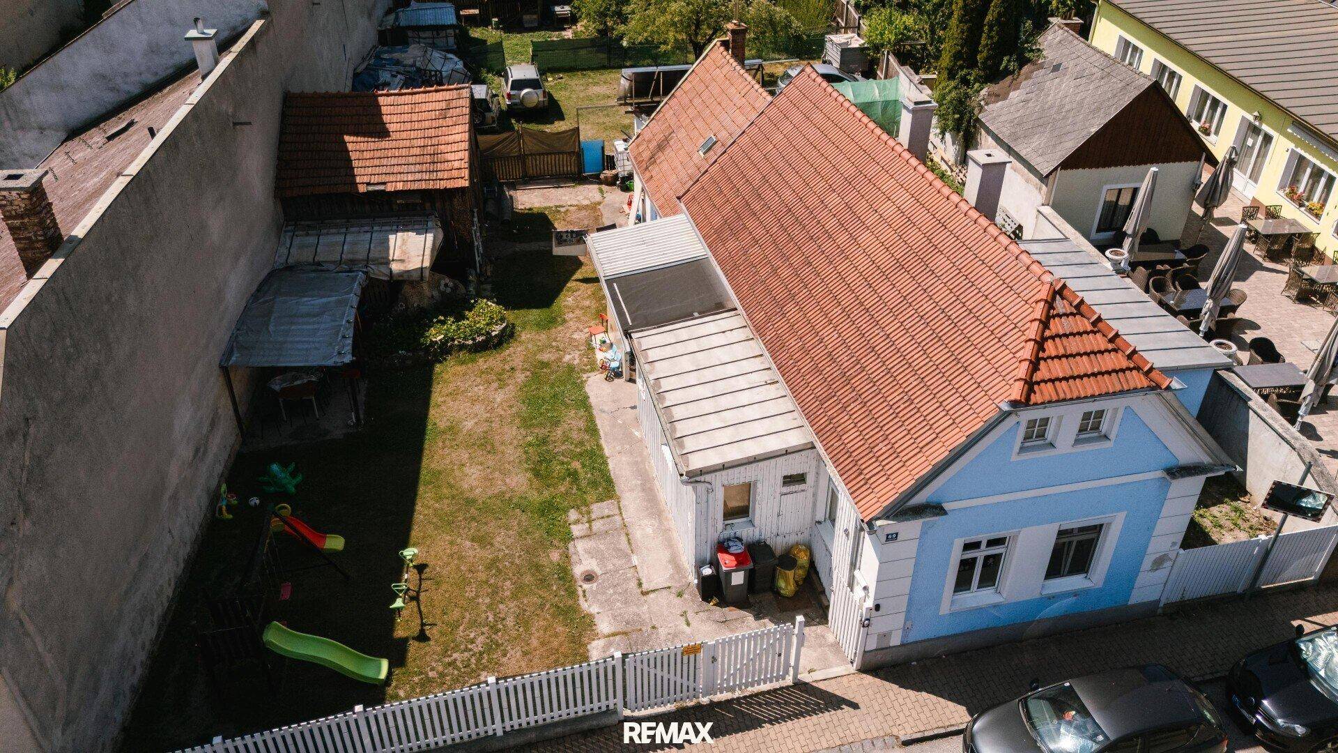 Luftaufnahme des Hauses mit Garten, Spielplatz und umliegenden Gebäuden unter blauem Himmel.