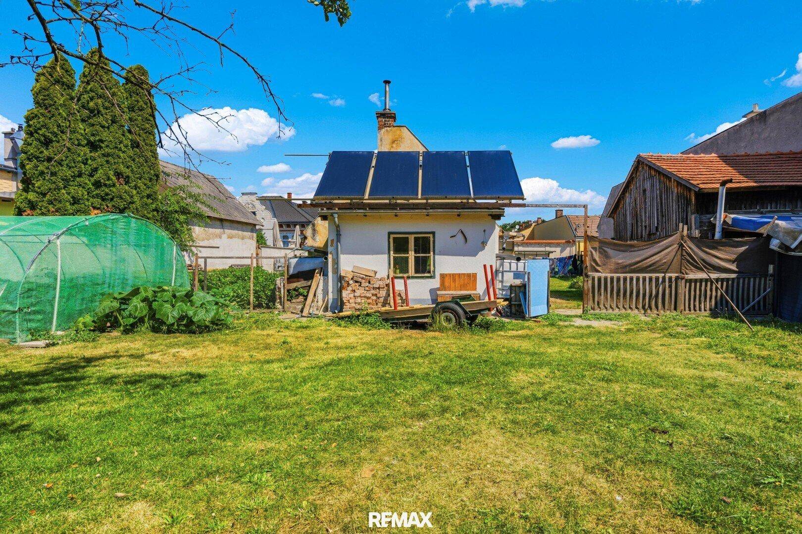 Großer Garten mit Rasenfläche, kleinem Nebengebäude und Solaranlage auf dem Dach.