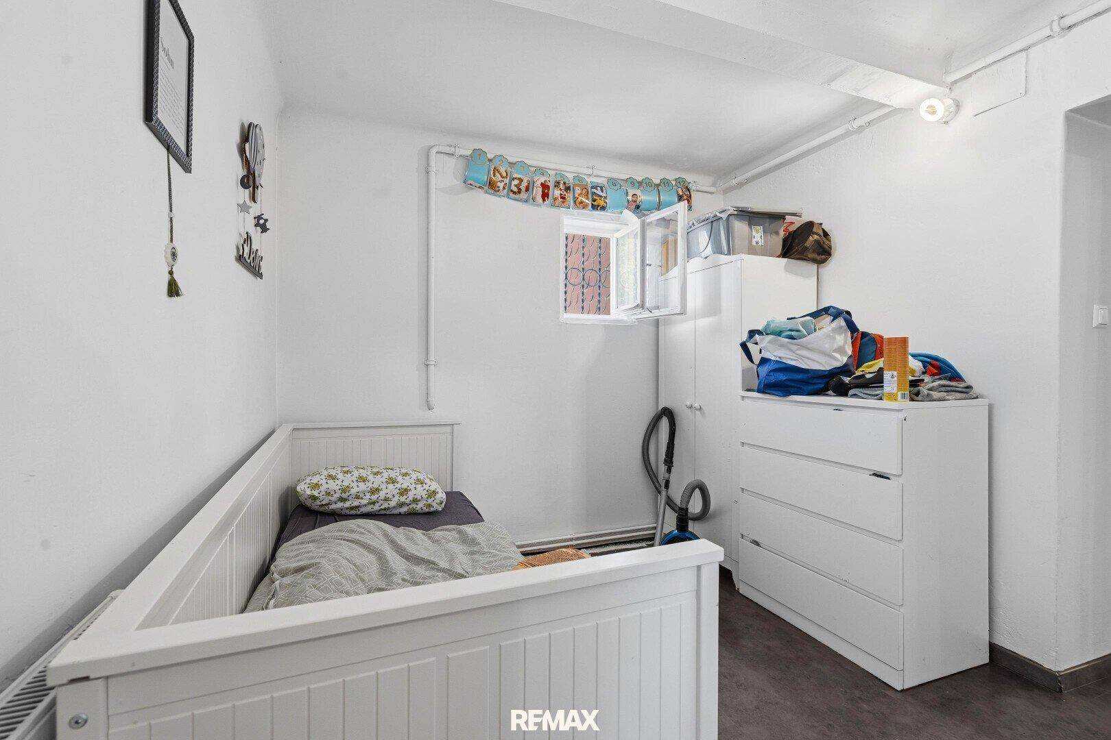 Kinderzimmer mit Einzelbett, Kommode und kleinem Fenster, ideal für ein Kind.