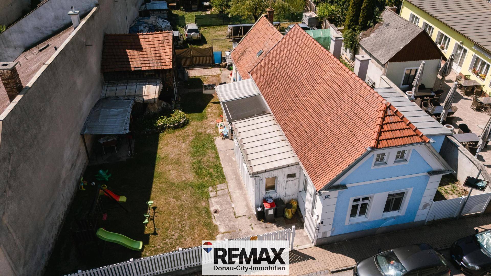 Luftaufnahme des blauen Hauses mit rotem Ziegeldach und großem Gartenbereich mit Spielgeräten.
