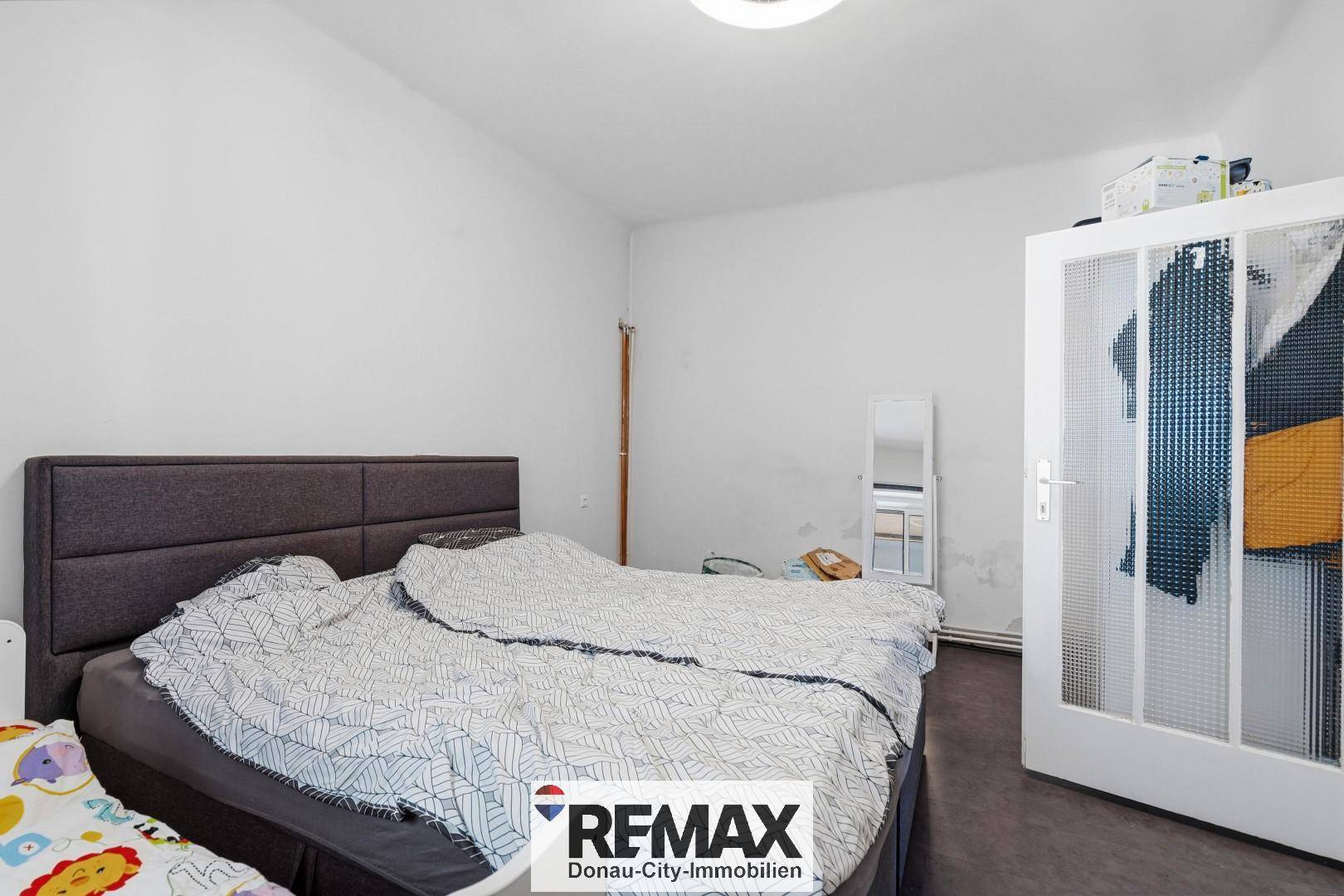 Schlafzimmer mit Doppelbett, weißem Kleiderschrank und dunklem Bodenbelag in schlichtem Design.
