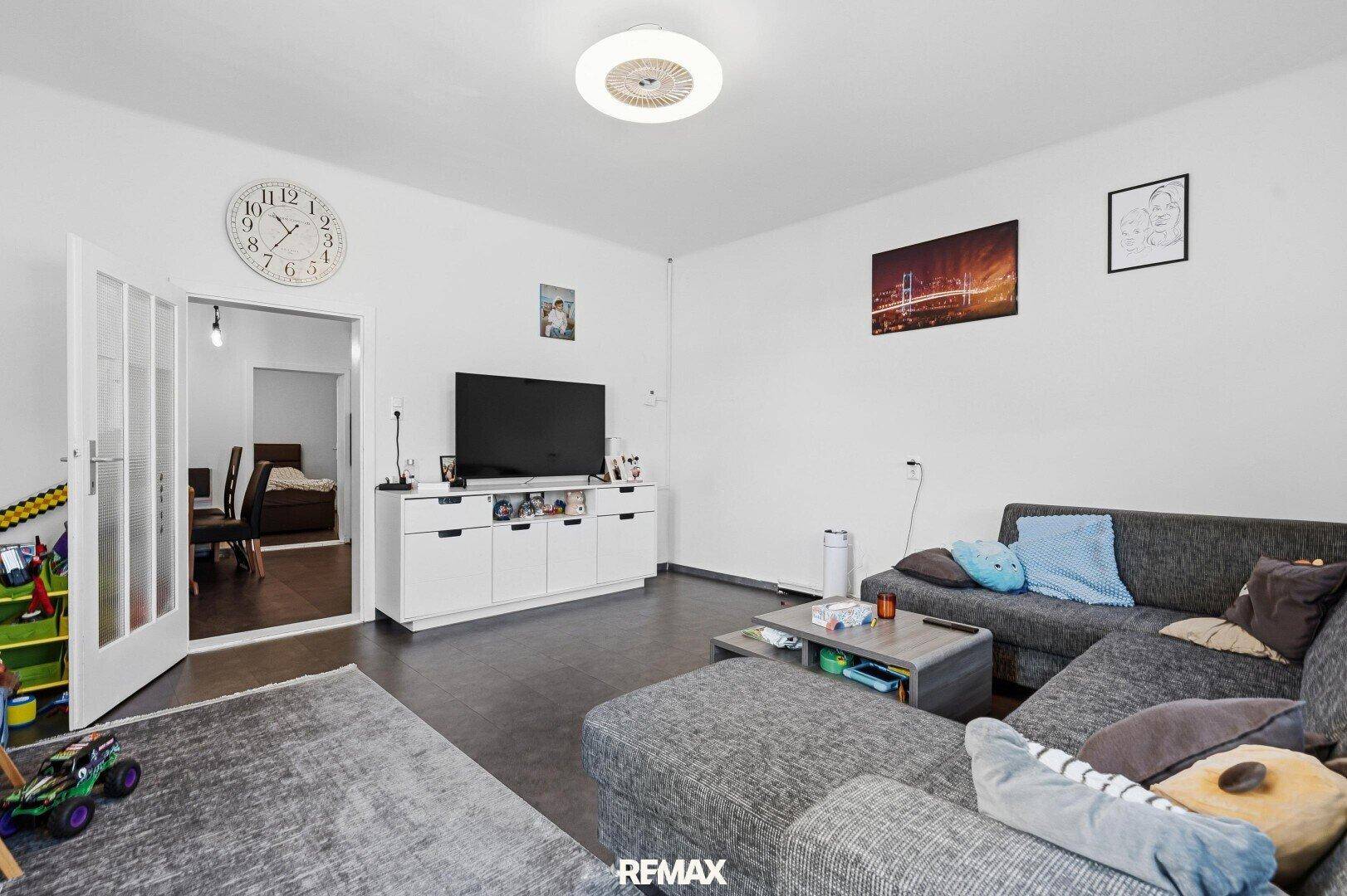 Gemütliches Wohnzimmer mit großem Ecksofa, Fernseher und Zugang zu einem weiteren Raum.