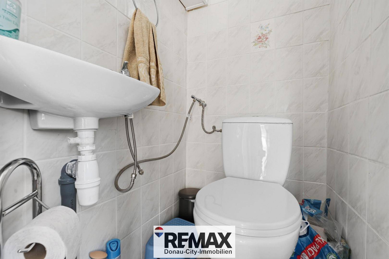 Kleines WC mit Toilette, Waschbecken und hellen Fliesen an den Wänden.