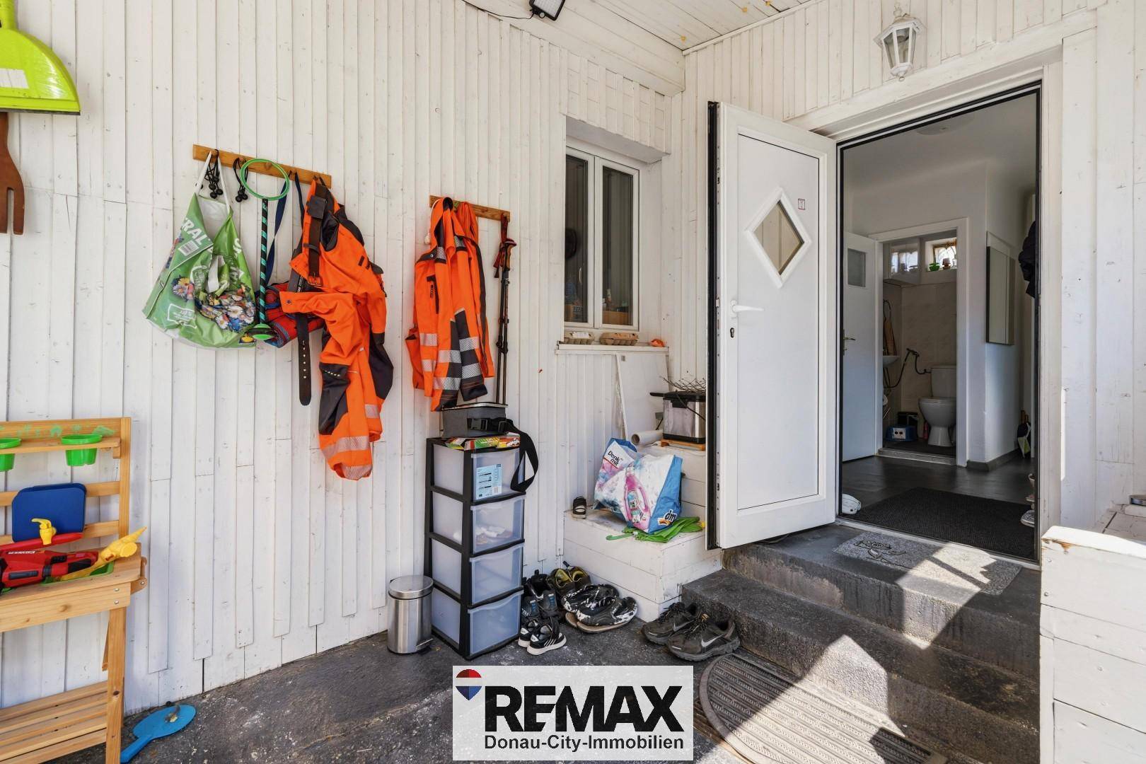 Überdachter Eingangsbereich mit Holzwänden, Garderobe und Zugang zum Inneren des Hauses.