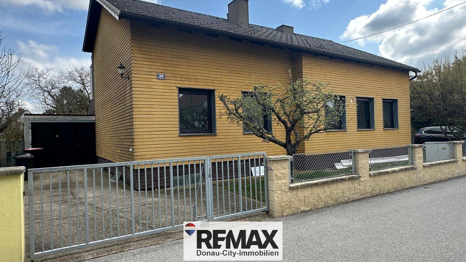 Vorderansicht des Hauses mit gelber Holzfassade, Einfahrt und Carport auf der linken Seite.