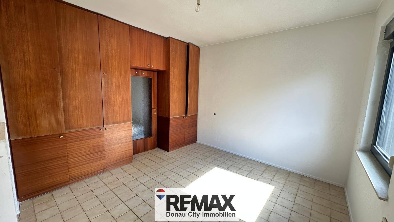 Schlafzimmer mit großen Einbauschränken aus Holz und Fliesenboden.