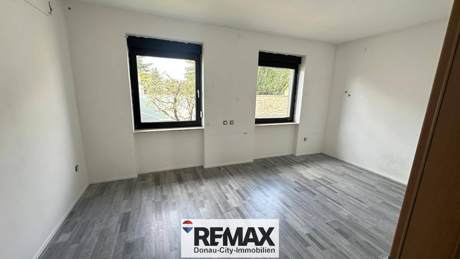 Renoviertes Zimmer mit neuem Laminatboden und zwei Fenstern für viel Licht.