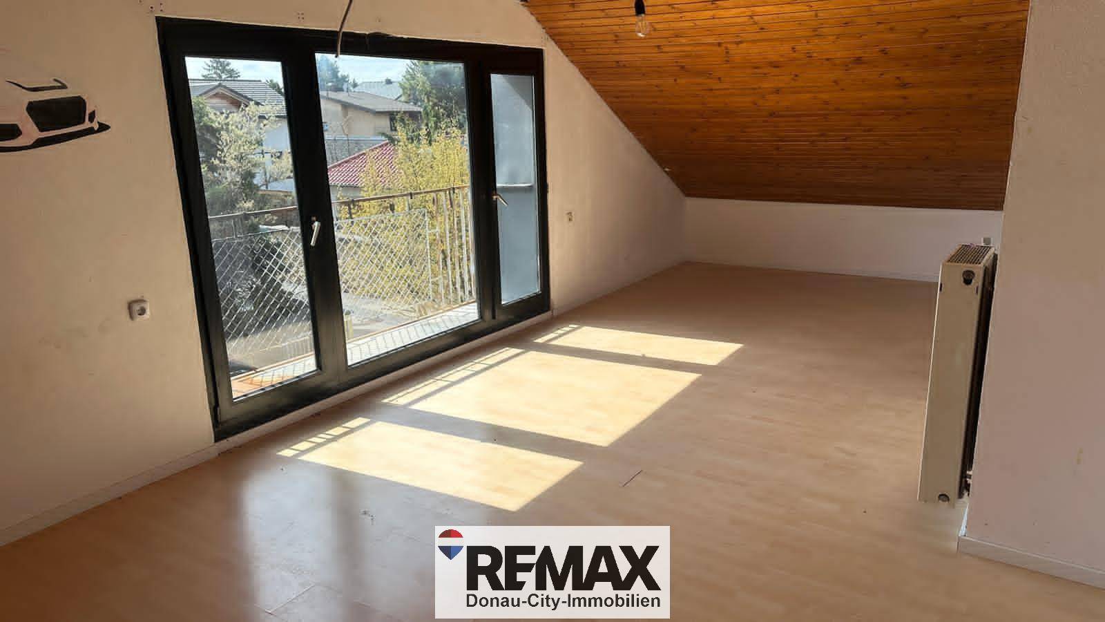 Helles Zimmer im Dachgeschoss mit Holzbalkendecke, Parkettboden und Zugang zum Balkon.
