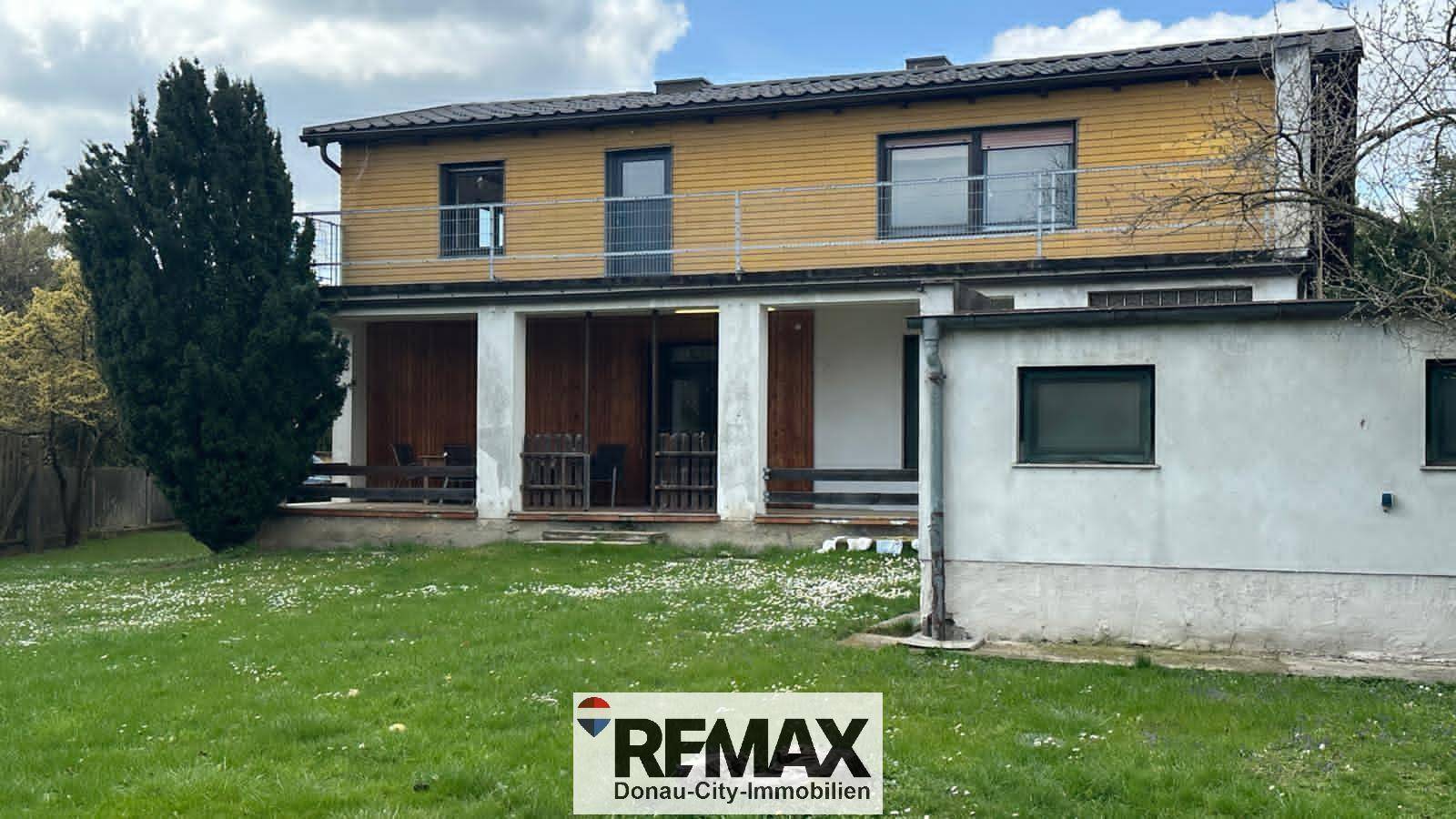 Weitläufiger Gartenbereich hinter dem Haus mit überdachter Terrasse und Balkon im Obergeschoss.