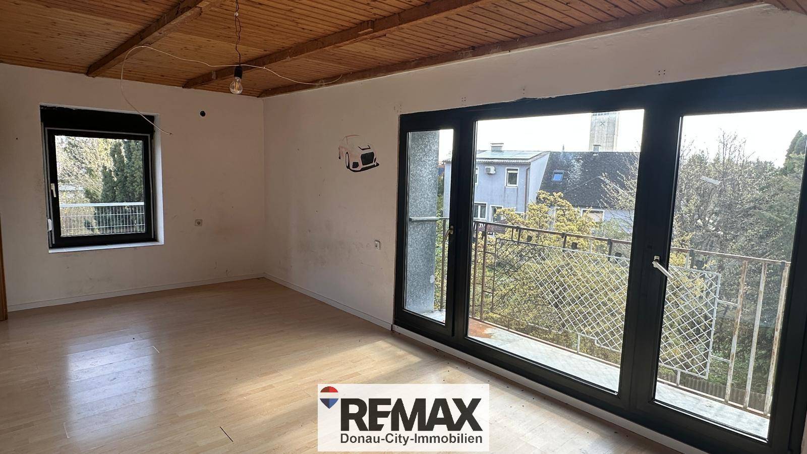 Helles Zimmer mit Holzbalkendecke, Parkettboden und Zugang zu einem französischen Balkon.