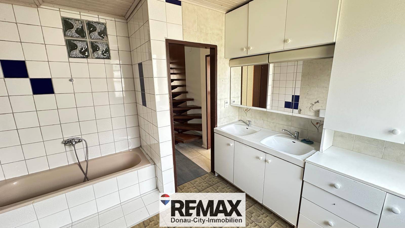 Badezimmer mit Badewanne, Doppelwaschbecken und Zugang zum Treppenhaus.