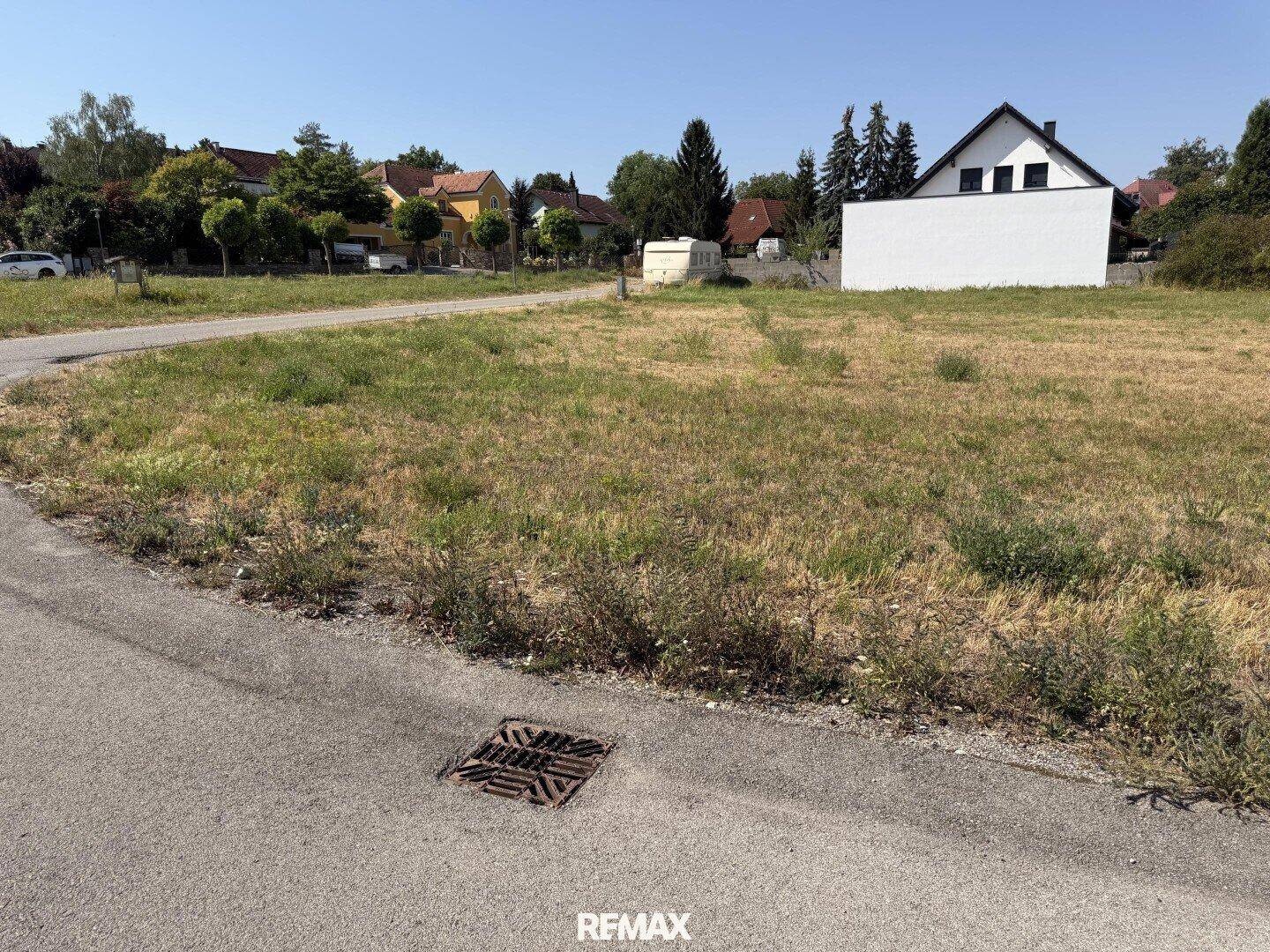 Blick auf das unbebaute Grundstück von der Straße aus, umgeben von Wohnhäusern.