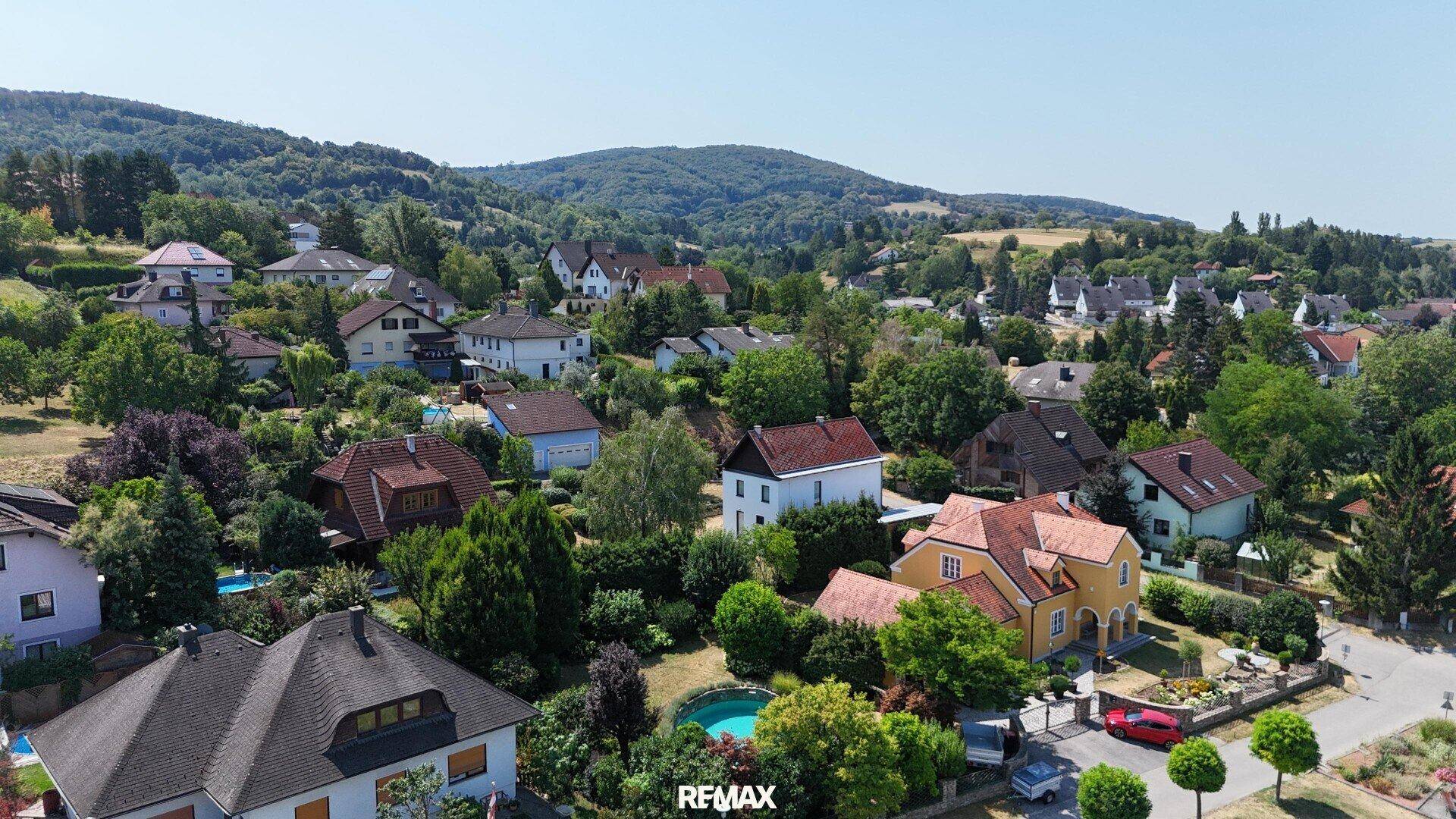 Panoramablick aus der Vogelperspektive auf eine grüne Wohnsiedlung in hügeliger Landschaft.
