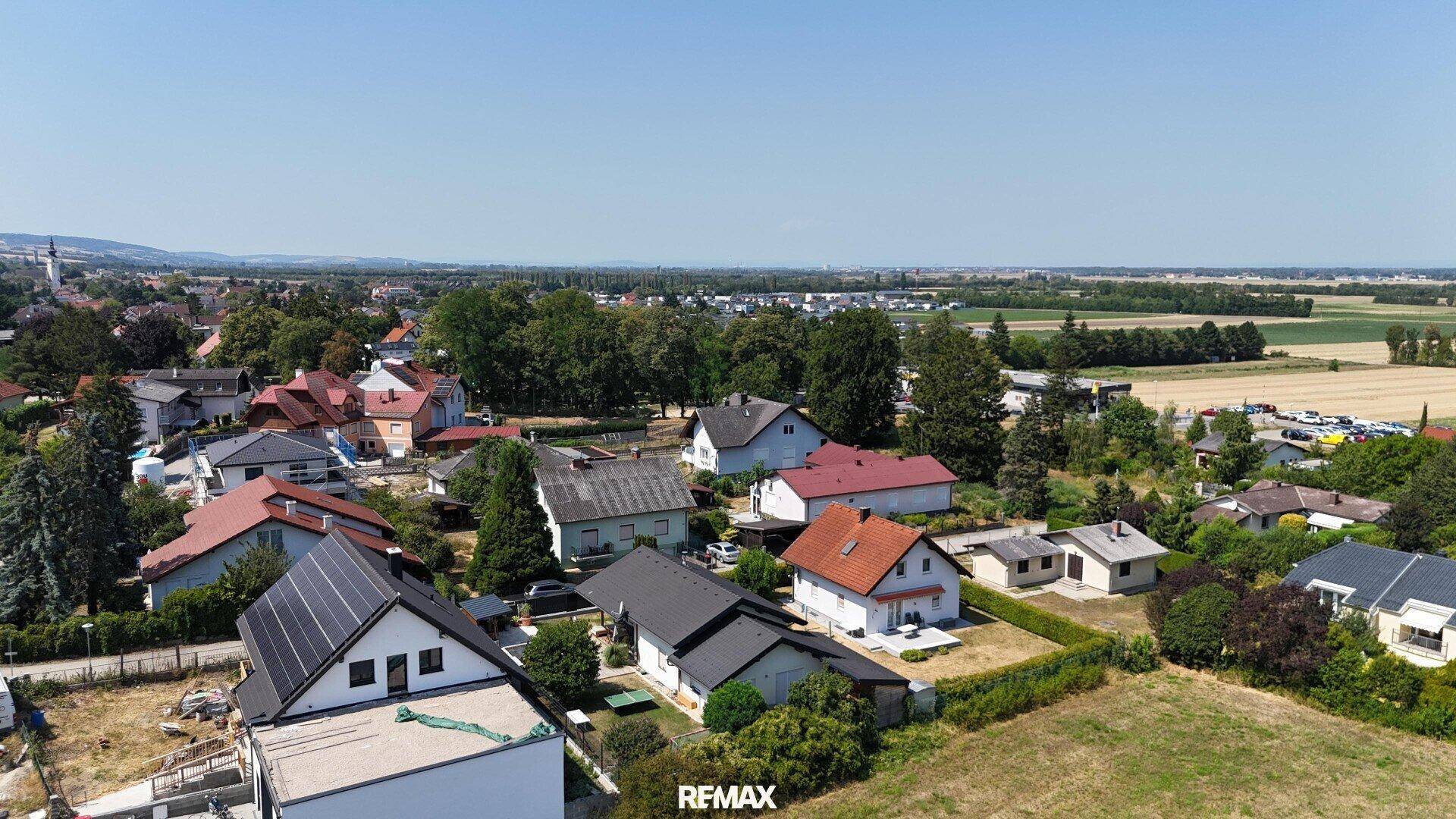 Weitläufige Luftaufnahme einer Wohnsiedlung mit Feldern und Bergen in der Ferne.