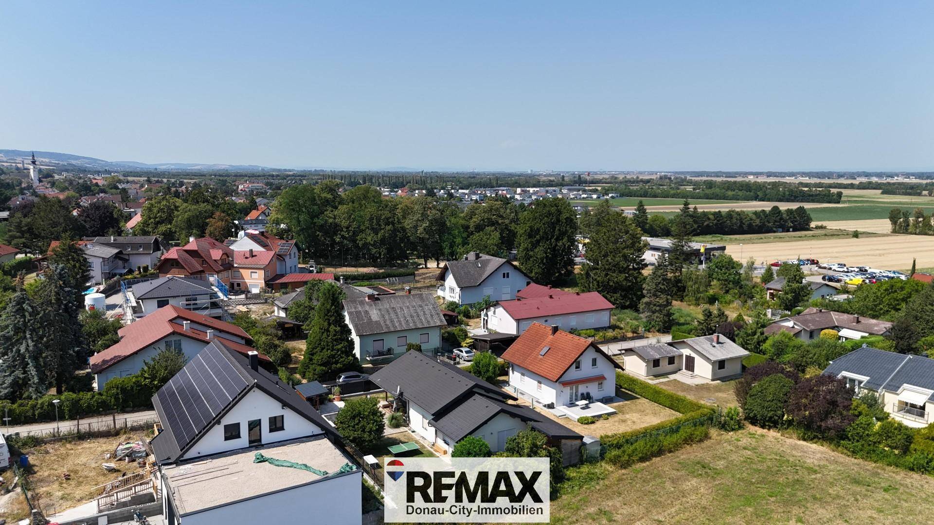 Weitläufige Luftaufnahme einer Wohnsiedlung mit vielen Häusern und Feldern im Hintergrund.