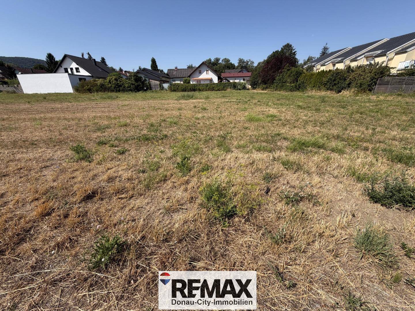 Weitläufiges, unbebautes Grundstück mit trockenem Gras und Blick auf die umliegende Wohnbebauung.