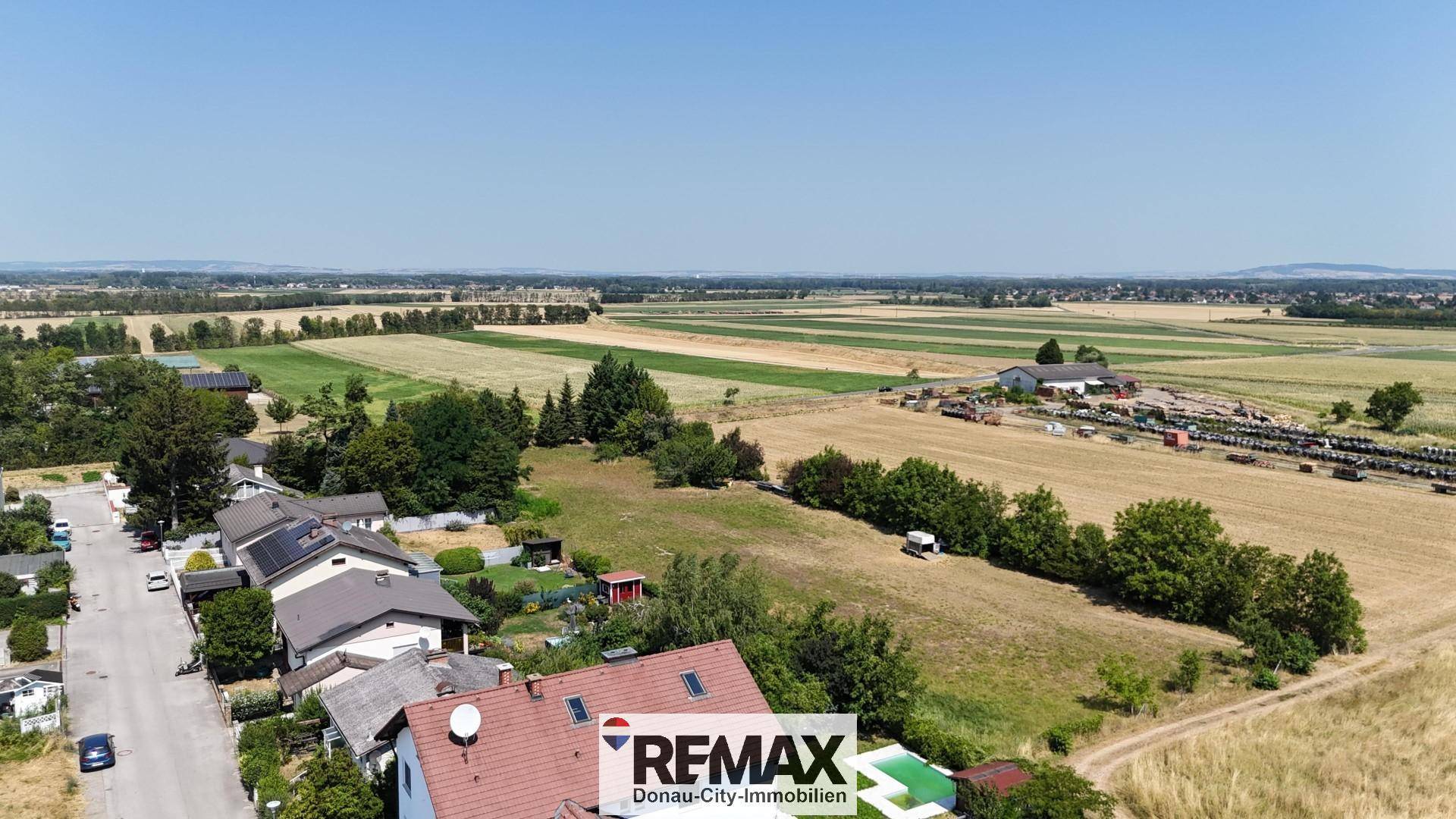 Panoramablick über eine ländliche Wohnsiedlung mit weiten Feldern und klarem Himmel.