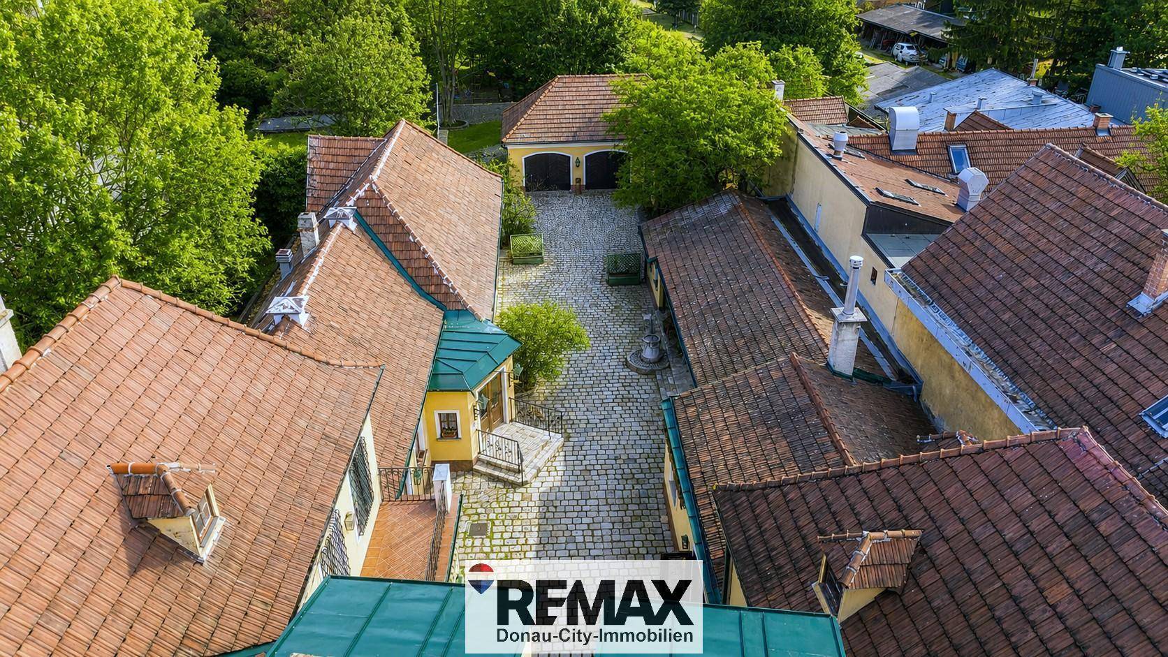 Luftaufnahme eines weitläufigen Gebäudekomplexes mit mehreren Dächern und einem Innenhof.