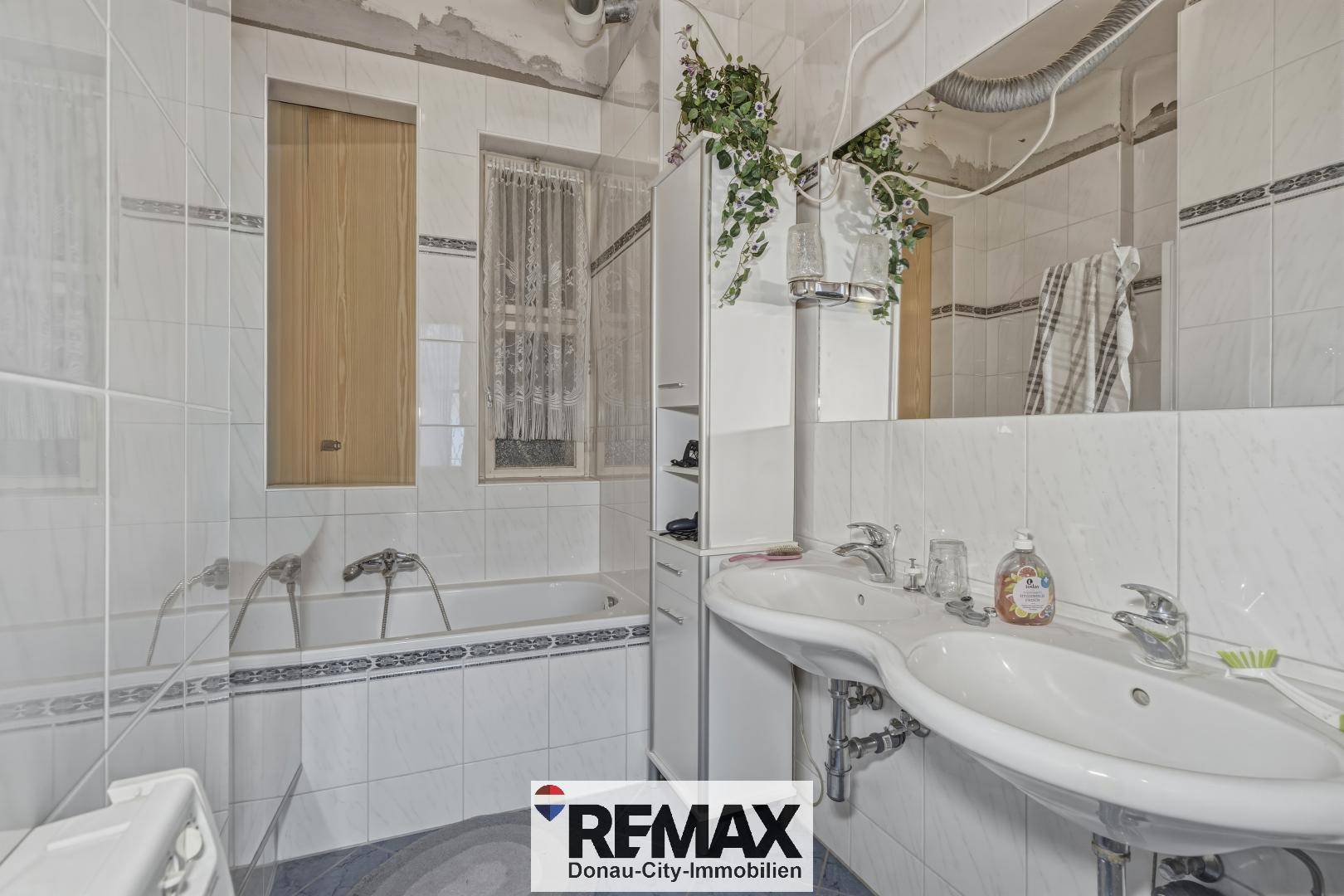 Gefliestes Badezimmer mit Badewanne, Doppelwaschbecken und Spiegelschrank.