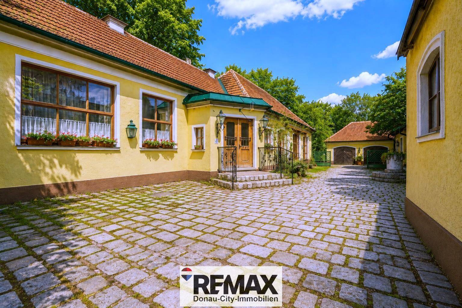Gepflasterter Innenhof mit einem historischen Gebäude und üppiger grüner Vegetation.