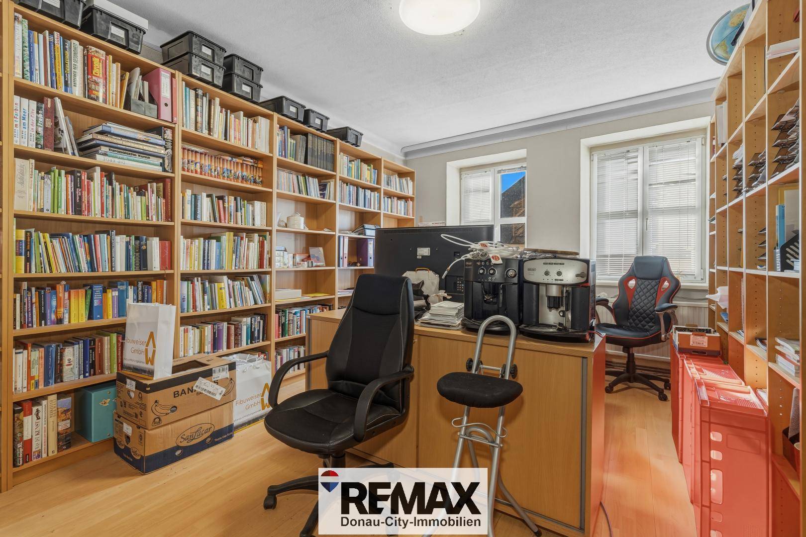 Helles Arbeitszimmer mit raumhohen Bücherregalen und zwei Schreibtischen.