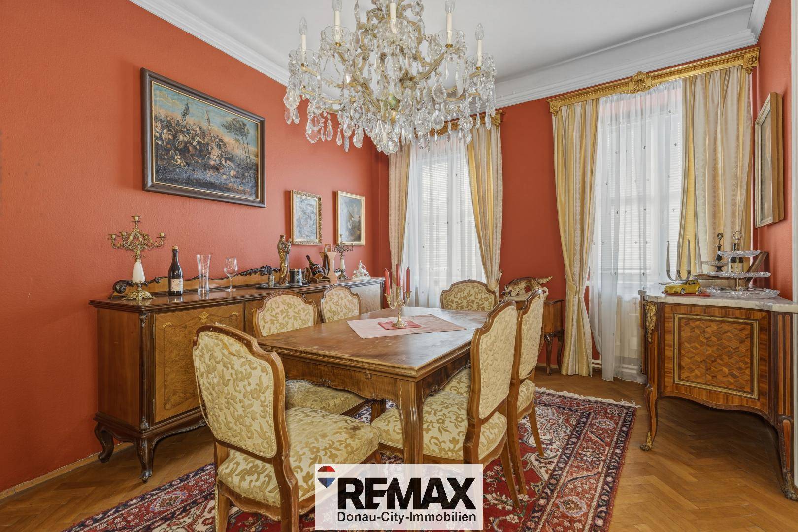 Elegantes Esszimmer mit roter Wandfarbe, Kronleuchter und antiken Holzmöbeln.