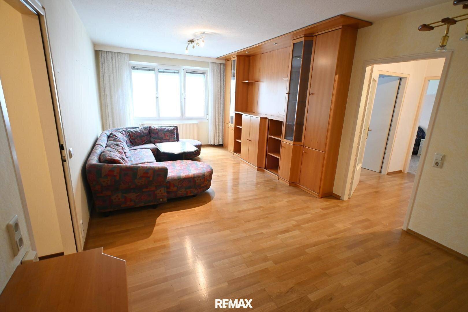 Gemütliches Wohnzimmer mit Ecksofa, Holzschrankwand und Parkettboden, einladend gestaltet.