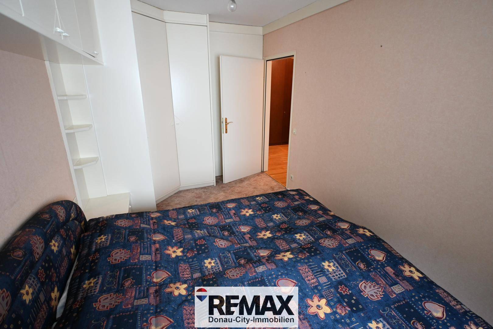 Schlafzimmer mit Teppichboden und weißen Einbauschränken, Zugang zu weiterem Raum.